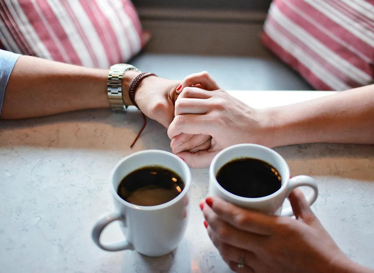 Two people holding hands across a table during a serious conversation